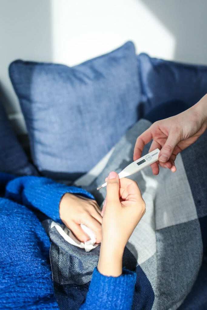 pexels photo 3873186 A woman checks her temperature using a digital thermometer while resting on a couch at home.